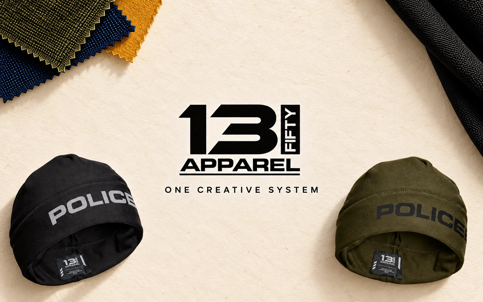 Flat lay on cream paper: a black and an olive-green 13 Fifty POLICE beanie, fabric swatches and the 13 Fifty Apparel logo with the line “One creative system”.