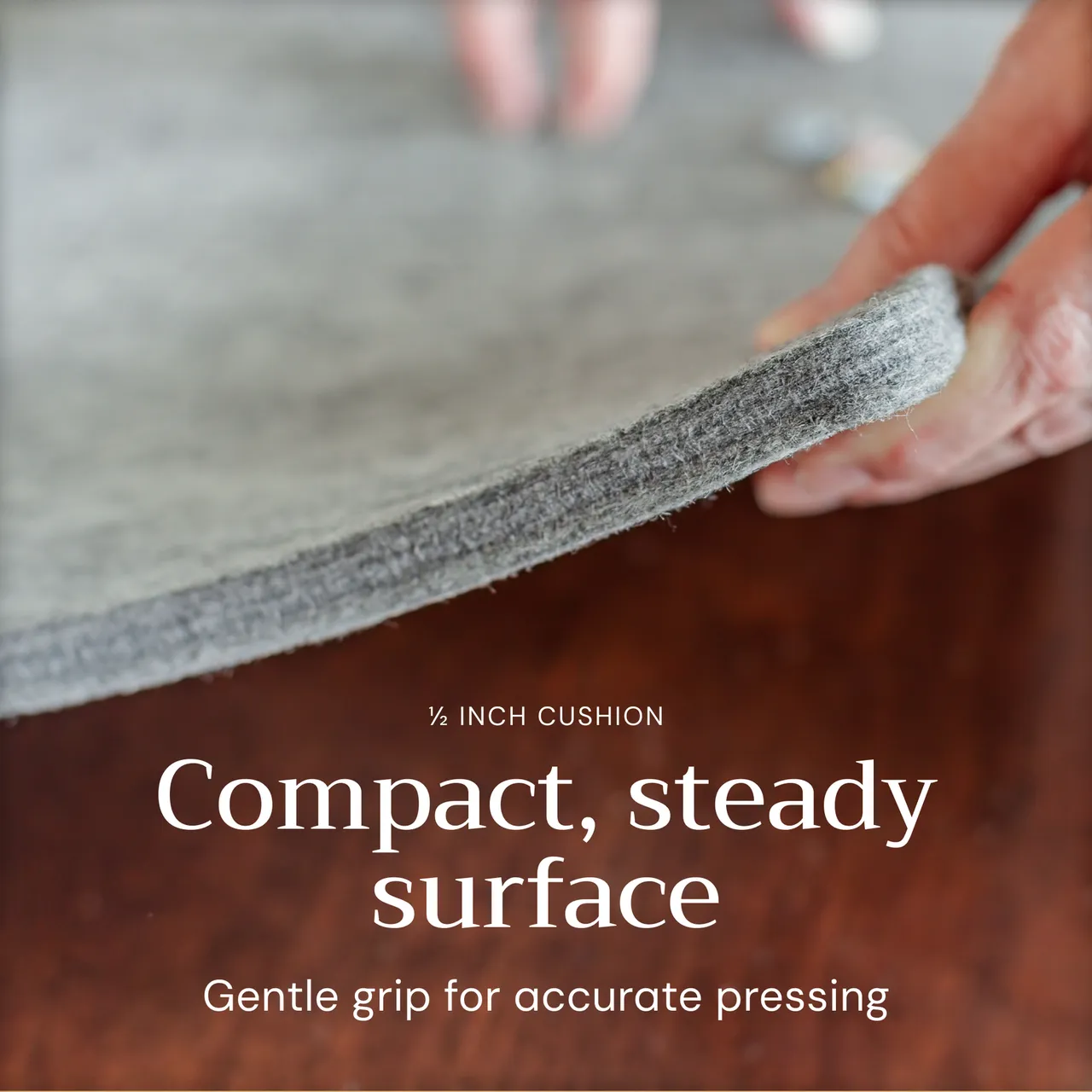 Close-up of a hand lifting the edge of the Novodon wool pressing mat to show its thickness and felt texture.